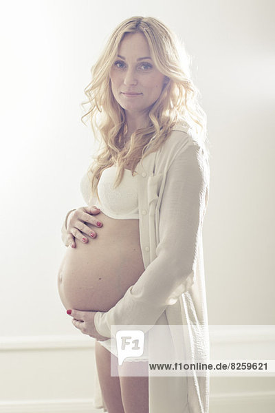 Porträt einer schwangeren Frau  die den Bauch zu Hause hält.