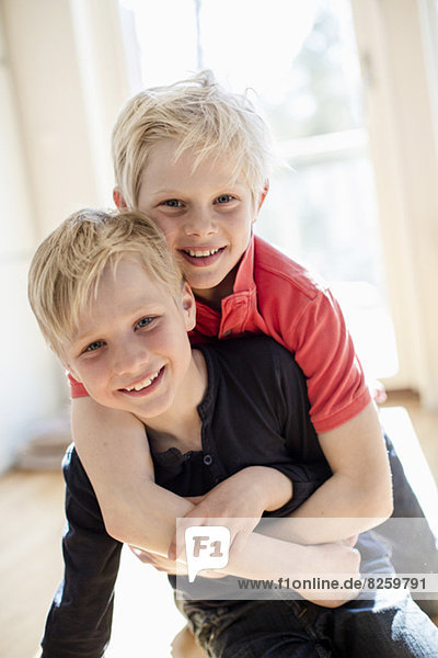 Portrait of boy embracing brother from behind in house