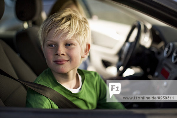 Lächelnder kleiner Junge  der durch das Autofenster schaut.