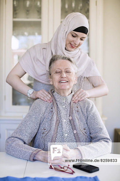 Young female home caregiver giving shoulder massage to grandmother at home
