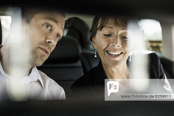 Happy businesswoman sitting with colleague in taxi
