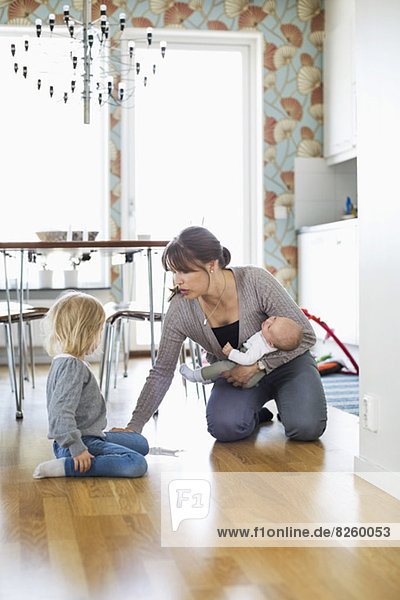 Mother holding baby while cleaning floor with daughter at home