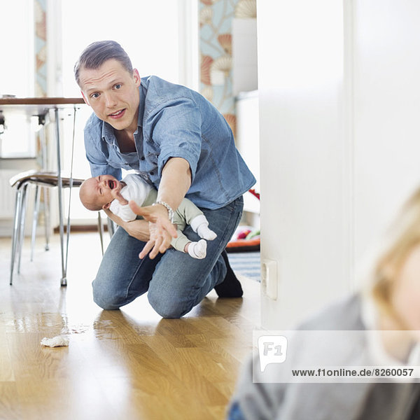 Vater hält weinendes Baby  während er die Tochter zu Hause auf dem Boden hält.