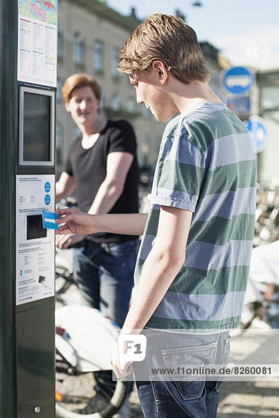 Junger Mann bezahlt mit Kreditkarte beim Fahrrad-Sharing-System