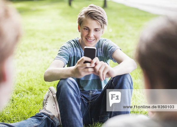 Glücklicher junger Mann beim Fotografieren von Freunden im Park