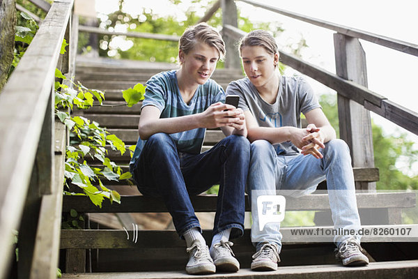 Junge männliche Freunde mit dem Handy auf der Treppe im Freien