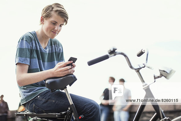 Junger Mann  der mit dem Handy auf dem Fahrrad auf der Straße sitzt.