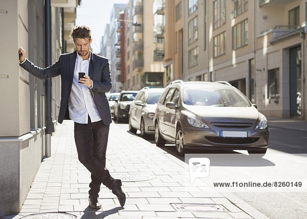 Volle Länge der jungen Geschäftsmann mit Handy auf dem Bürgersteig