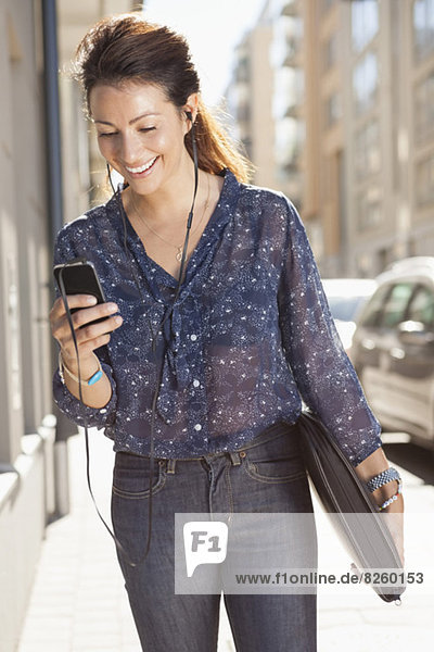 Fröhliche Geschäftsfrau beim Musikhören mit dem Handy auf dem Bürgersteig