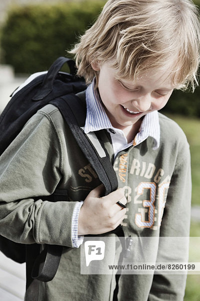 Kleiner Schuljunge mit Rucksack lächelnd im Freien