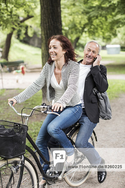 Geschäftsfrau auf dem Fahrrad mit Kollegin über Handy auf dem Rücksitz