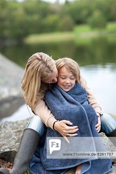 Mother drying son with towel at lake