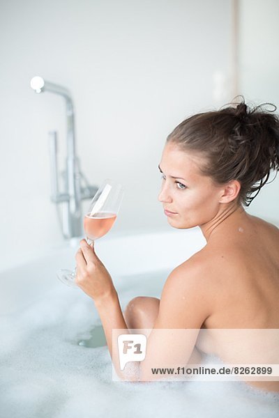 Young woman having bath with glass of wine