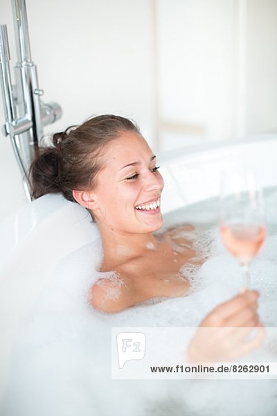Young woman having bath and drinking wine