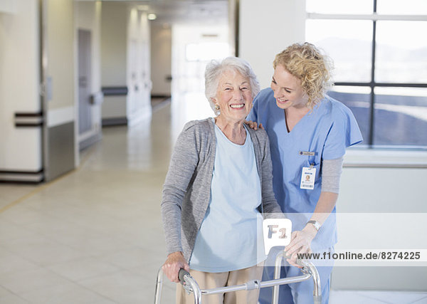 Krankenschwester hilft älteren Patienten mit Gehhilfe im Krankenhausflur