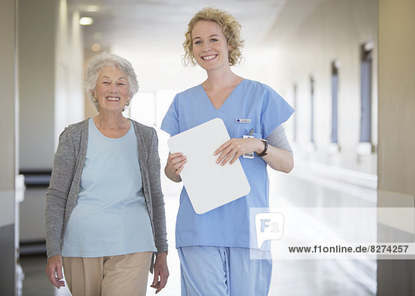 Portrait of smiling nurse and senior patient in hospital corridor