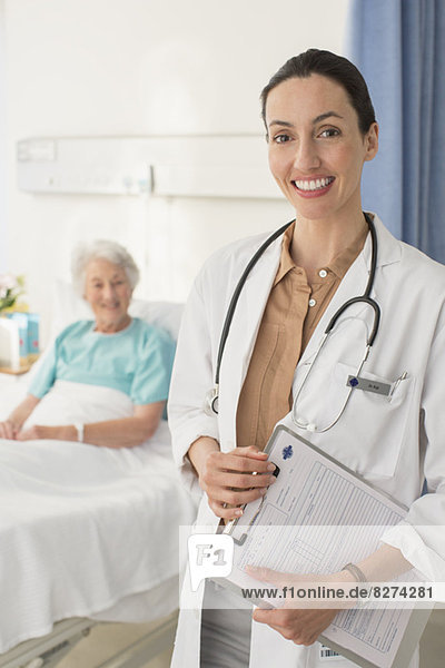 Porträt eines lächelnden Arztes mit einem älteren Patienten im Hintergrund