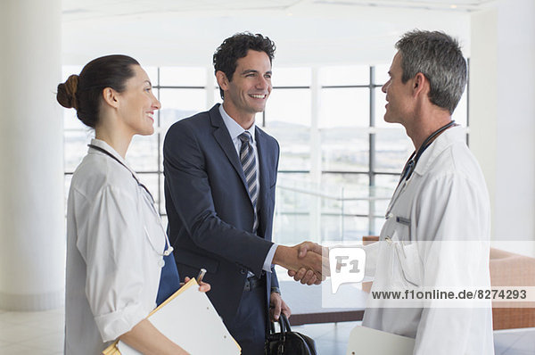 Doctor and businessman handshaking in hospital lobby