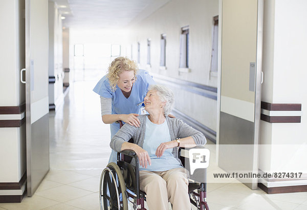 Krankenschwester mit alternder Patientin im Rollstuhl im Krankenhausflur