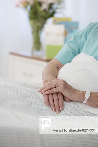 Nahaufnahme der Hände eines älteren Patienten im Krankenhausbett