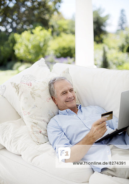 Senior Mann online einkaufen auf der Terrasse Sofa