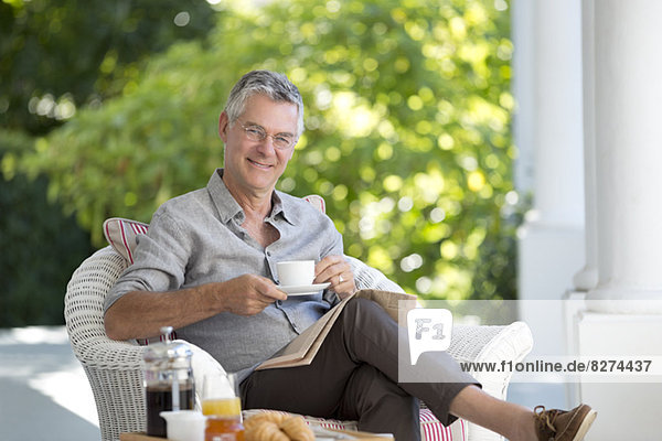 Porträt eines lächelnden älteren Mannes beim Kaffeetrinken auf der Terrasse