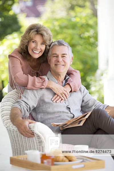 Porträt eines lächelnden älteren Paares  das sich auf der Terrasse umarmt.