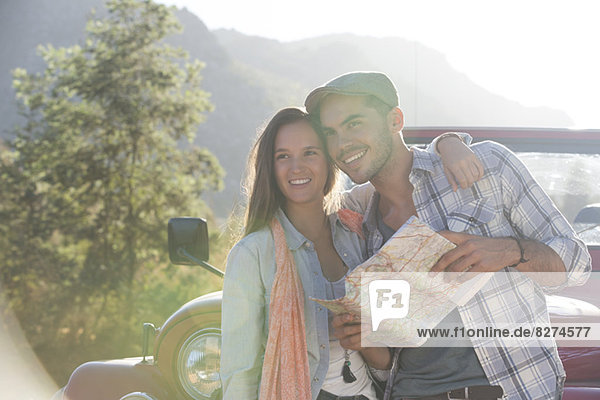 Lächelndes Paar mit Karte neben dem Geländewagen