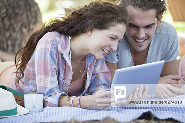 Paar mit digitalem Tablett auf Decke im Freien