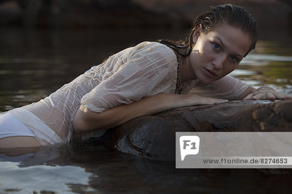 Portrait einer sinnlichen Frau  die auf einem Felsen im Fluss liegt.