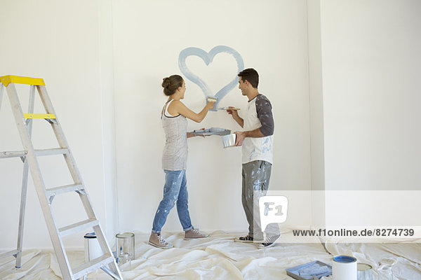 Couple painting blue heart on wall