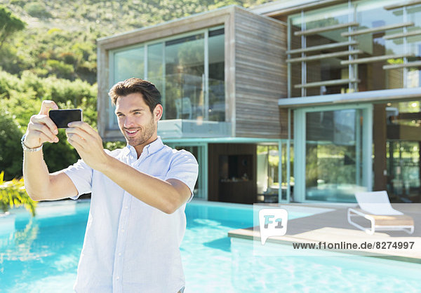 Man taking self-portrait with camera phone at poolside