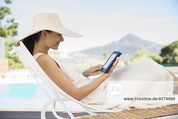 Frau mit digitalem Tablett auf Liegestuhl am Pool