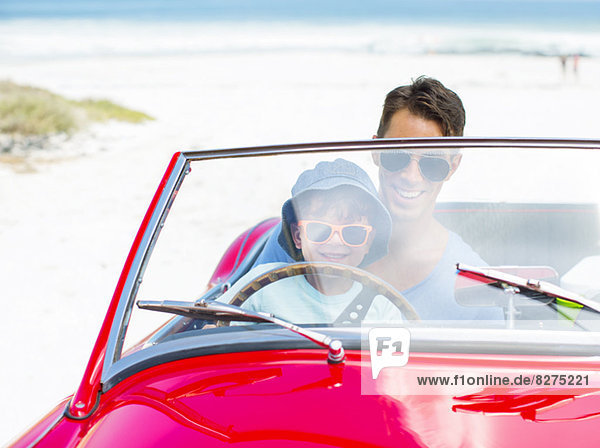 Father and son driving convertible on beach