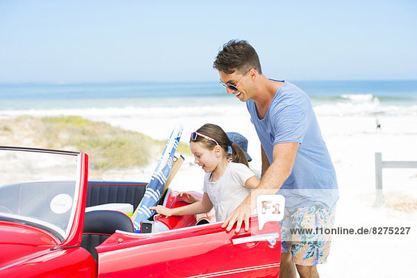 Father helping daughter into convertible on beach