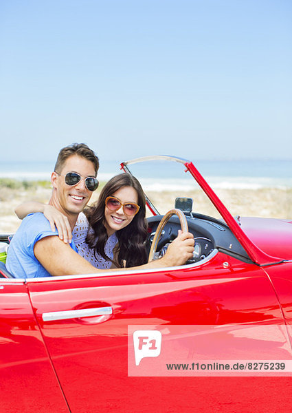 Couple driving convertible at beach