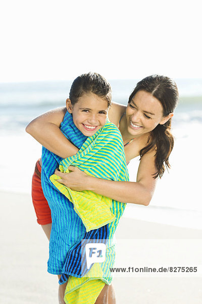 Mother wrapping daughter in towel on beach