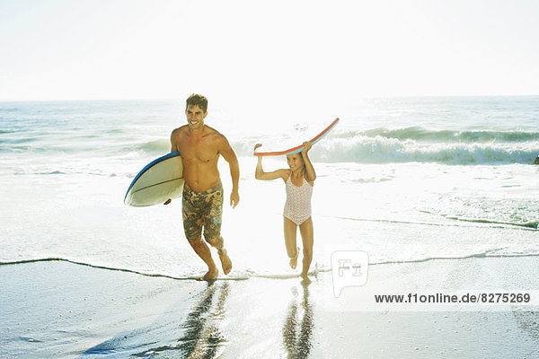 Father and daughter carrying surfboard and bodyboard on beach