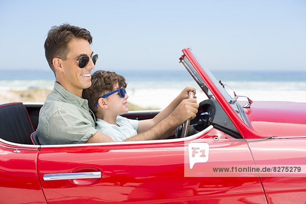 Father and son driving convertible at beach
