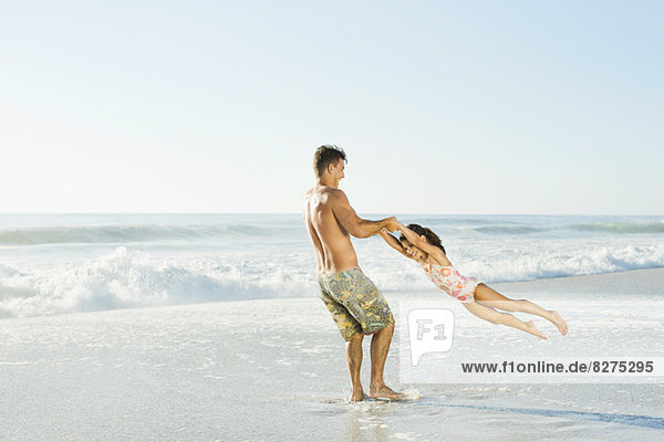 Father swinging daughter in surf at beach