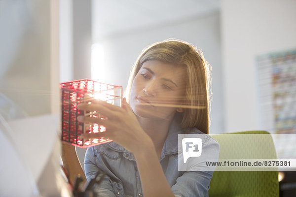 Businesswoman examining cube at desk in office