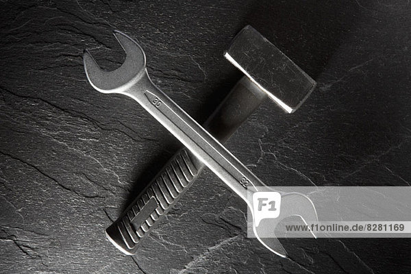 Ein Schraubenschlüssel  der auf einem auf einer Granitplatte liegenden Schlägerhammer balanciert.