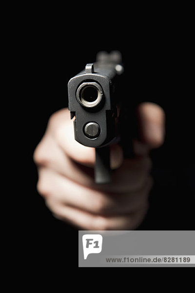 A hand holding a gun and pointing it at the camera  black background