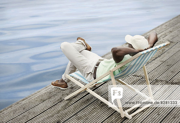 Man relaxing by lake on deck chair