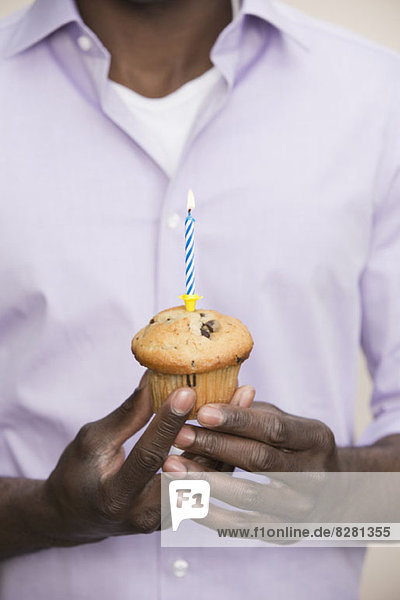 Mann hält Muffin mit einzelner Kerze oben drauf