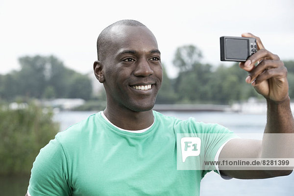 Smiling man taking photograph of himself by lake