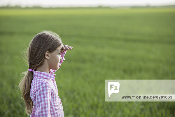 Ein junges Mädchen steht auf einem Feld  schirmt ihre Augen ab und schaut auf den Blick.