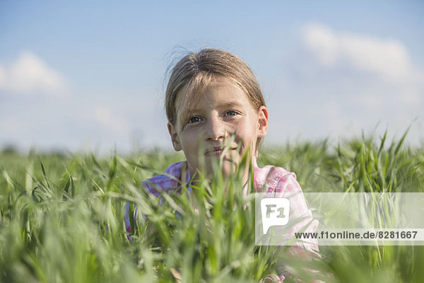 Ein junges lächelndes Mädchen  das an einem Sommertag im Gras liegt.