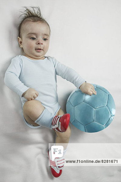 Ein kleiner Junge in Baby-Fußballschuhen  der auf einen Fußball zuschlägt.