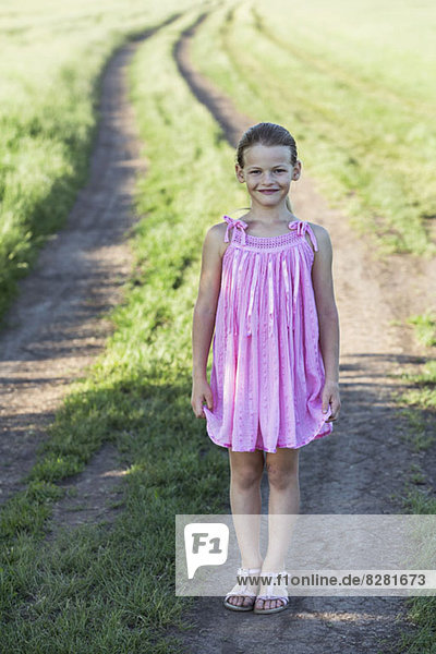 Ein junges lächelndes Mädchen  das auf einem Feldweg auf dem Land steht.
